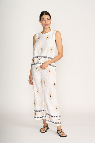 Woman wearing a white sleeveless top and pants with black patterns on a white background